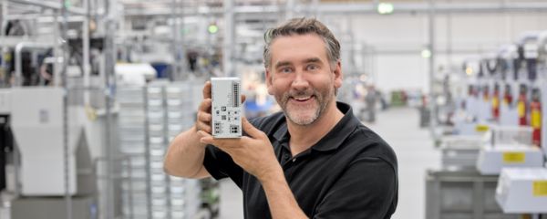 Person standing in a production hall, holding a UPS to the camera