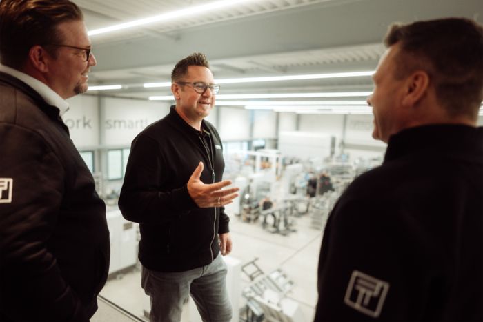 Phoenix&nbsp;Contact consultant with two Tobol employees in conversation with a view of the production hall