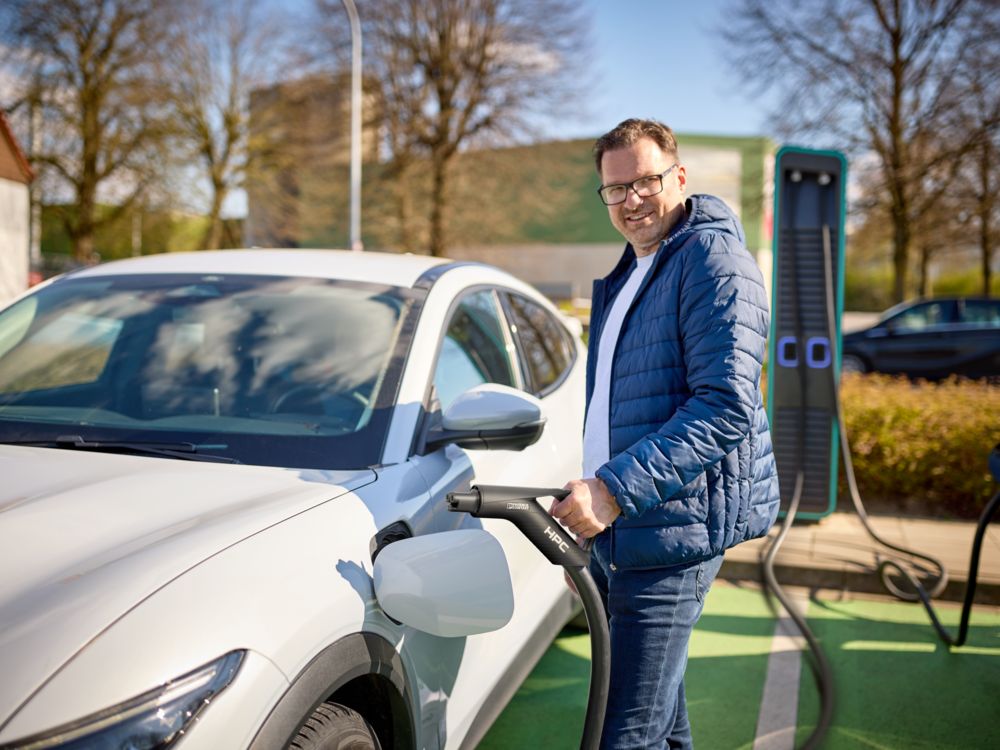 Un hombre carga su coche eléctrico mediante un cable de carga NACS en la estación de carga rápida