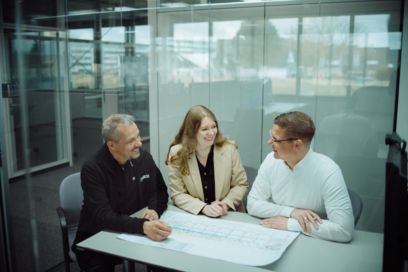 Drei Personen sitzen an einem Tisch in einem Bürogebäude