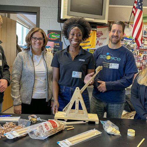 Five adults smiling, standing in a classroom in front of a table with various supplies and materials laid out