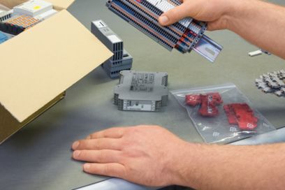 Eine Person sitzt am Tisch und hält eine bestückte Klemmenleiste in der Hand