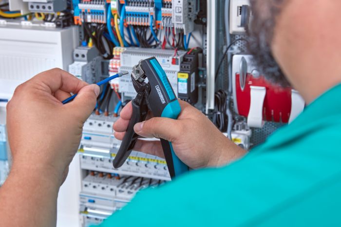 Person holding CRIMPFOX DUO 16S crimping pliers and a crimped conductor in front of a control cabinet