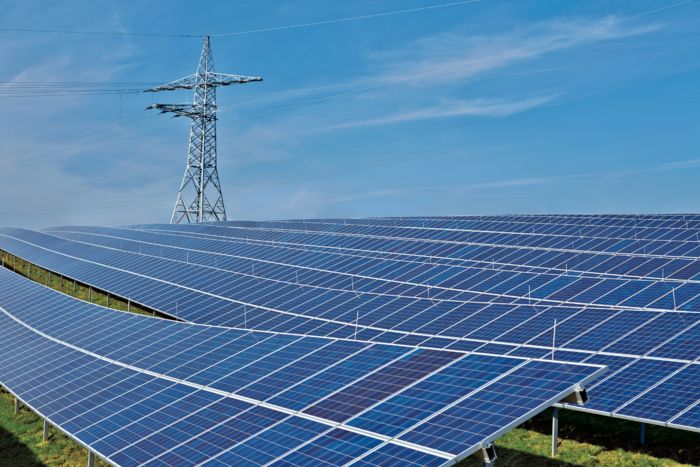 Rows of solar panels in a field on a sunny day, with power lines off in the distance