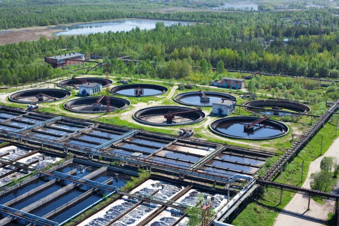 An aerial view of a water treatment plant on a bright sunny day, lush trees surround the plant
