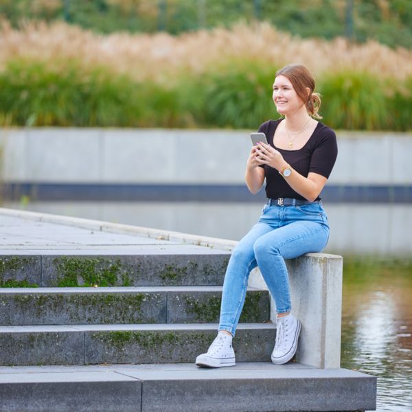 Auszubildende sitzt auf einer Mauer und hält ihr Handy in der Hand