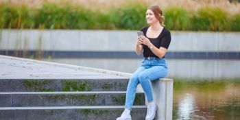 Auszubildende sitzt auf einer Mauer und hält ihr Handy in der Hand