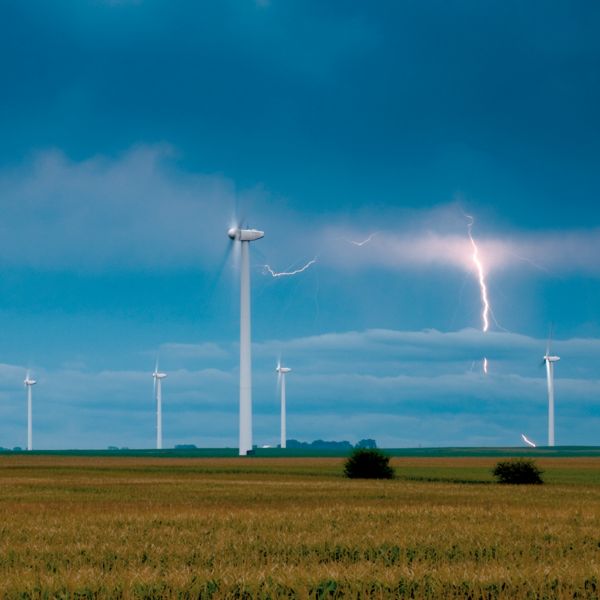 Plusieurs installations d'énergie éolienne dans un environnement rural avec des nuages orageux et des éclairs en arrière-plan