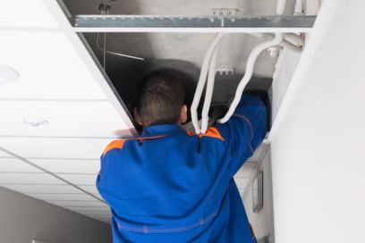 Installateur in einem Gebäude bei Überkopfarbeiten