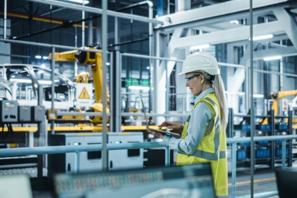 Frau mit Helm und Warnweste in einer Produktionshalle