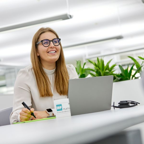 Mitarbeiterin arbeitet an einem Laptop und schaut in die Ferne