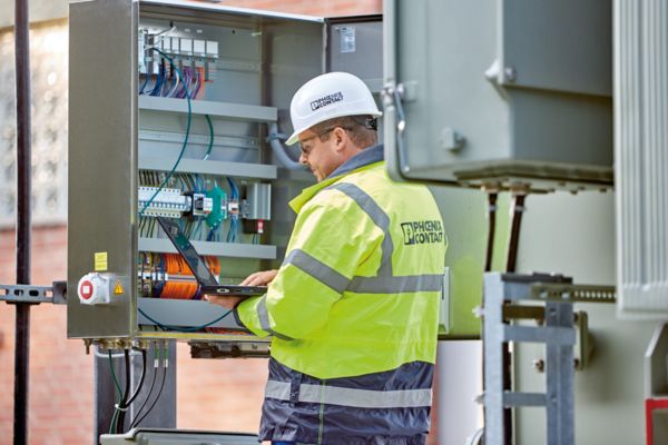 Hombre con ordenador portátil delante de un armario de control en la central eléctrica
