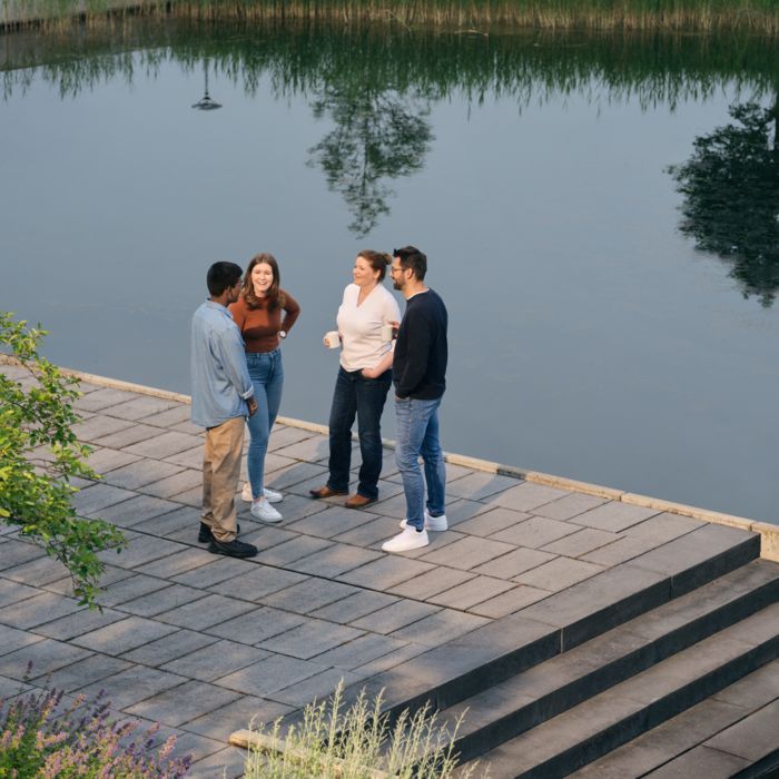 Mitarbeitende stehen am Wasser zusammen, unterhalten sich und trinken Kaffee