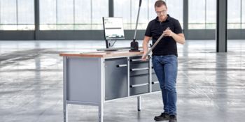Medewerker met ingekorte montagerail vóór een werkbank met montagerailfrees en monitor