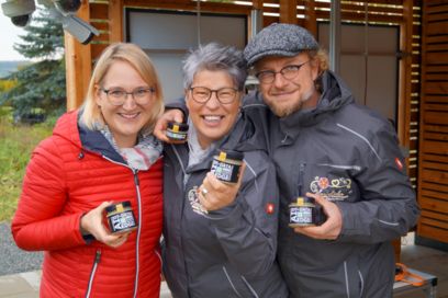 Three people standing next to each other holding a jar of honey