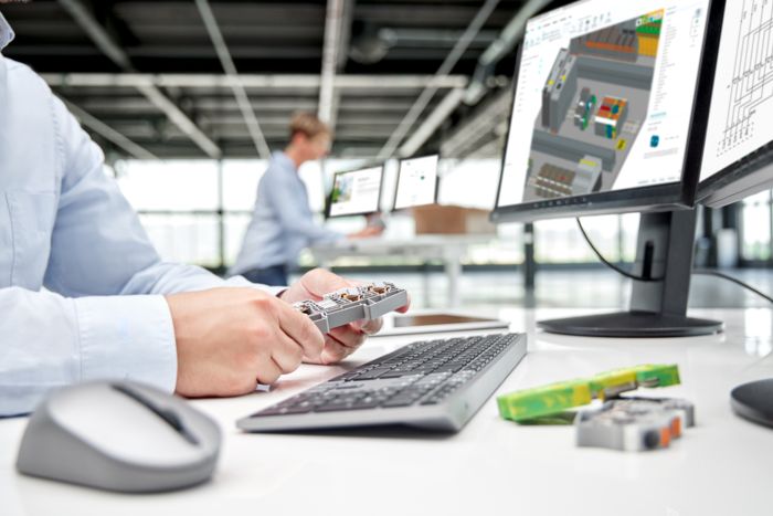 r Mão com uma régua de bornes em frente a um monitor com dados de engenharia