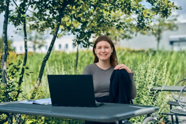 Junge Mitarbeiterin sitzt draußen an ihrem Laptop