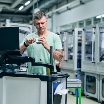 Mitarbeiter arbeitet in der Produktion und hält ein Produktionsteil in den Händen