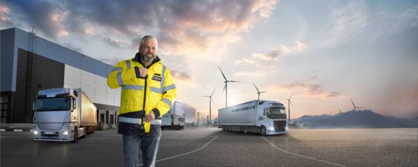 Mitarbeiter in Arbeitskleidung vor E-LKW und Windkraftanlagen