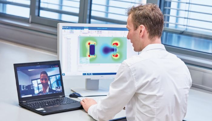 A man dressed in business attire sits at a desk in front of two monitors: a virtual meeting with woman is displayed on the left monitor, while a heatmap image is displayed on the right monitor.