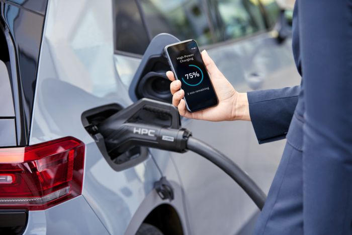 Charging cable plugged into an electric car and a person checking the charging status on a cellphone