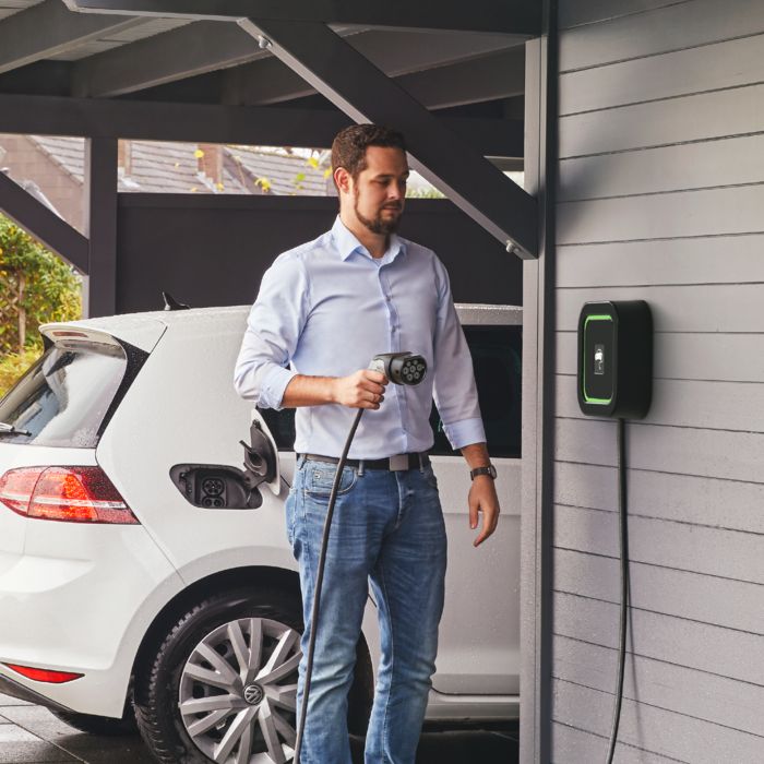 Electric car being charged in a carport at an AC home charger with a permanently attached charging cable