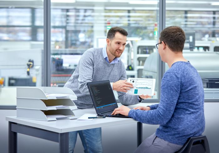 To mennesker i samtale rundt kravene til dataintegrering i en fabrikkhall