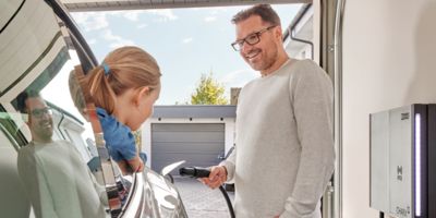 Une personne charge sa voiture électrique Tesla sur une borne de recharge murale à l'aide d'un câble de charge NACS