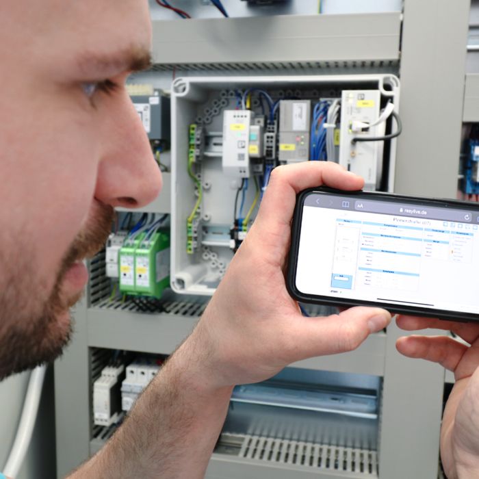 Un técnico observa la solución de portal web en su smartphone frente a un armario de control