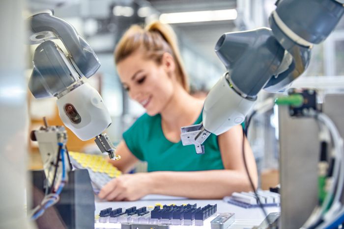 Woman and industrial robot collaborating on the production and testing of electronic components.