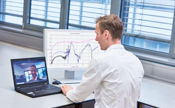 A man sits at a desk having a virtual meeting on his laptop with someone else, a chart is displayed on the desk next to the laptop