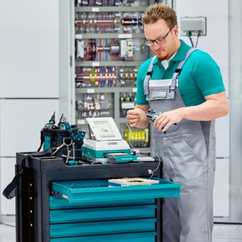Person in work trousers at a tool cart in front of a control cabinet