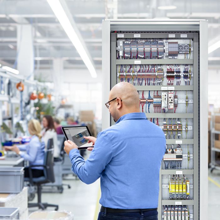 Person working with the clipx ENGINEER engineering software on a tablet in front of a control cabinet