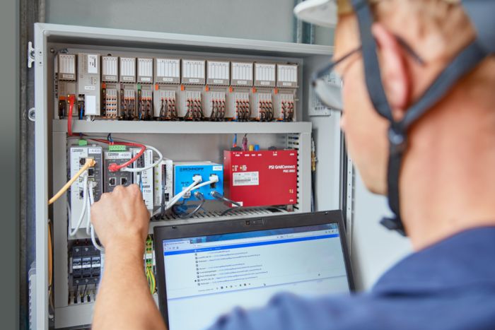 Person mit Laptop vor einem Schaltschrank