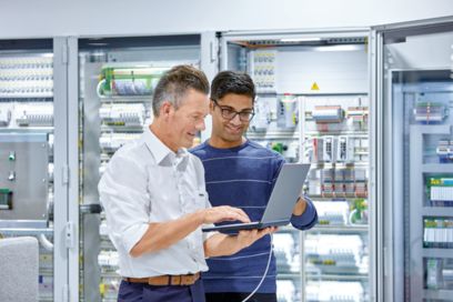 Two men with a laptop in front of a control cabinet