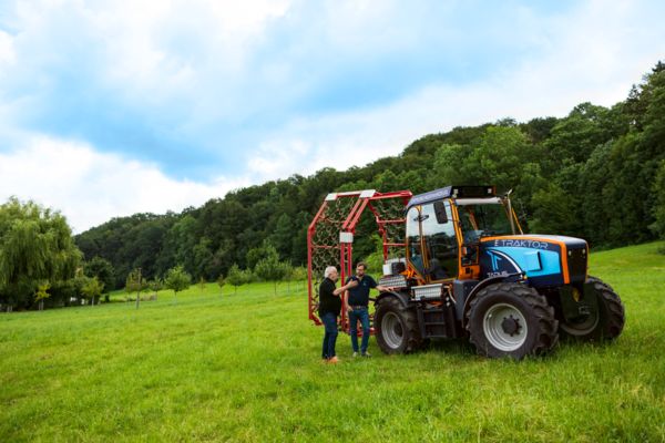 Deux personnes devant un tracteur électrique dans un paysage verdoyant
