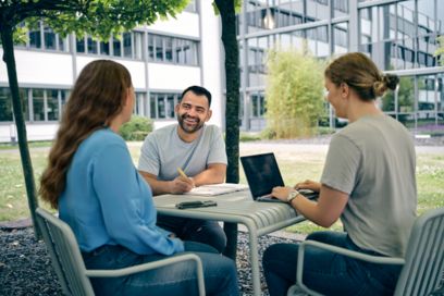 Mitarbeitende sitzen zusammen vor einem Bürogebäude und arbeiten zusammen
