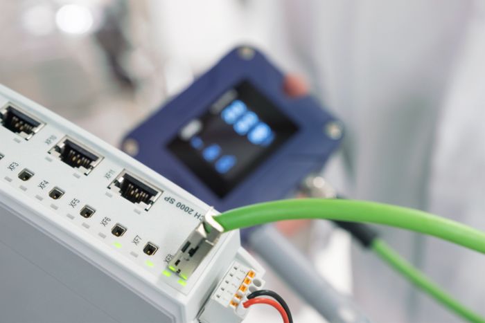 White Ethernet switch with a green SPE cable that connects a JUMO sensor in the background
