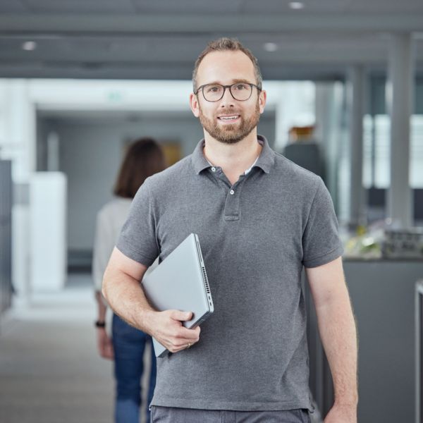 Ein Mitarbeiter steht mit einem Laptop unter seinem Arm in einem Büro